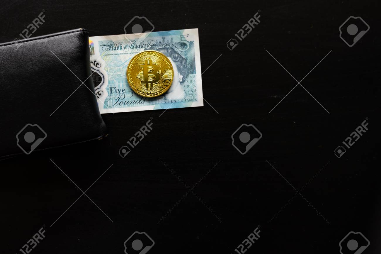 A Physical Bitcoin Sits On Top Of English Pounds Next To A Wallet - 